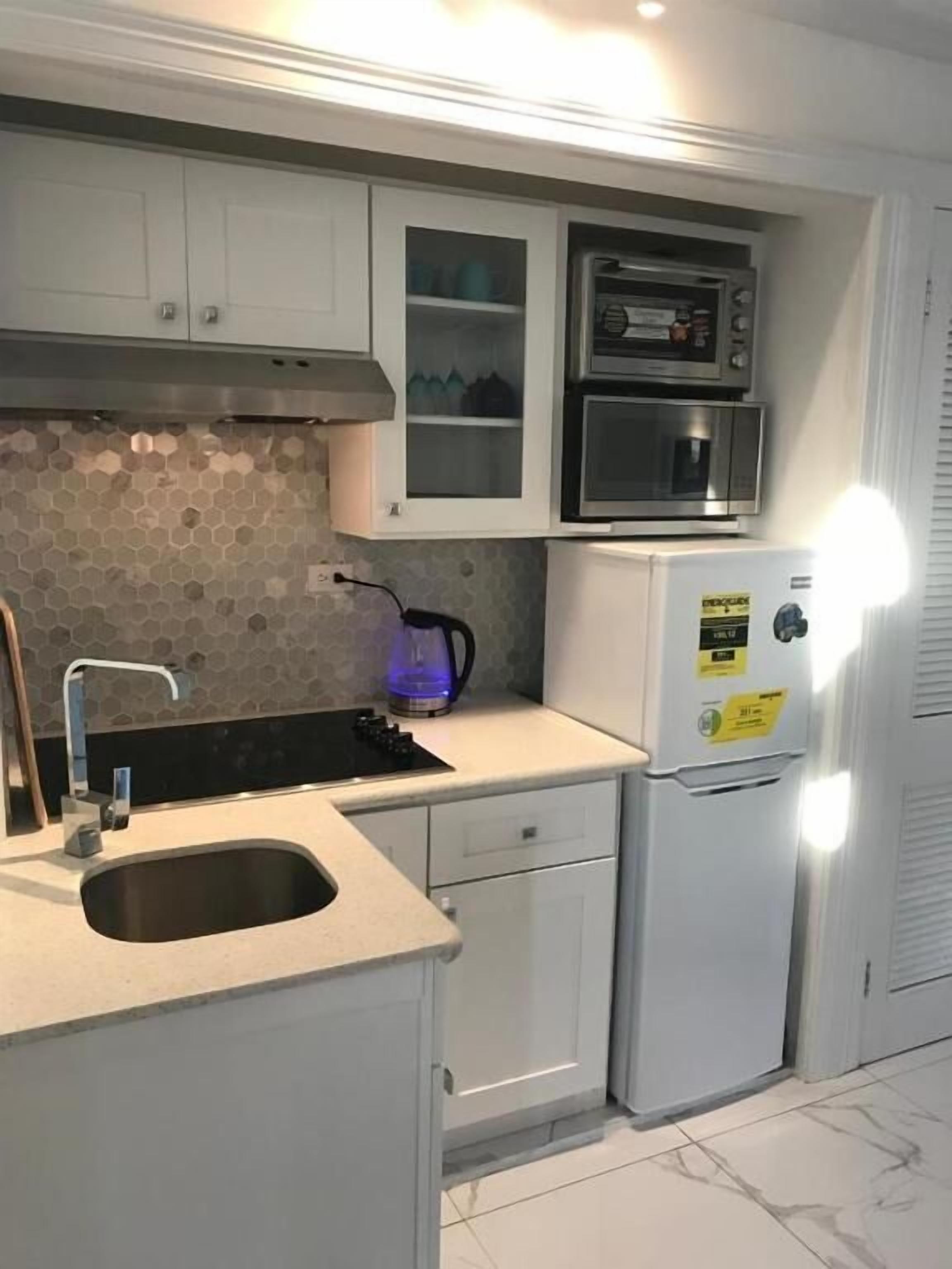 A kitchen with a built-in microwave, a kettle, and a refrigerator.