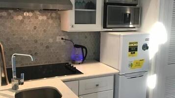 A kitchen with a built-in microwave, a kettle, and a refrigerator.