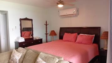 A bedroom with a bed, a nightstand, a dresser, a mirror, a ceiling fan, and an air conditioning unit.