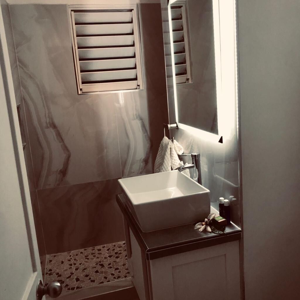 Een badkamer met een marmeren wand, een wastafel, een spiegel en een douche.
