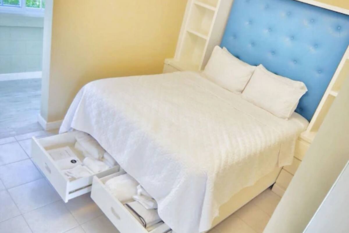 A neatly made bed with a blue headboard, white bedding, and a built-in storage drawer under the bed.
