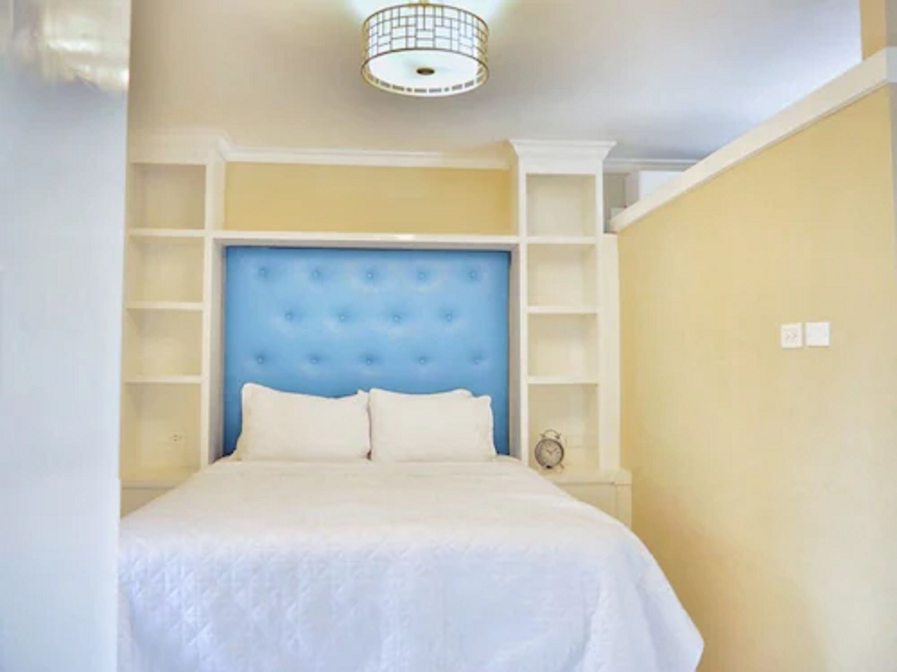 A bedroom with a tufted headboard, white bedding, and built-in shelving.
