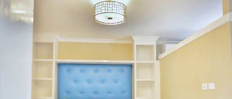 A bedroom with a tufted headboard, white bedding, and built-in shelving.