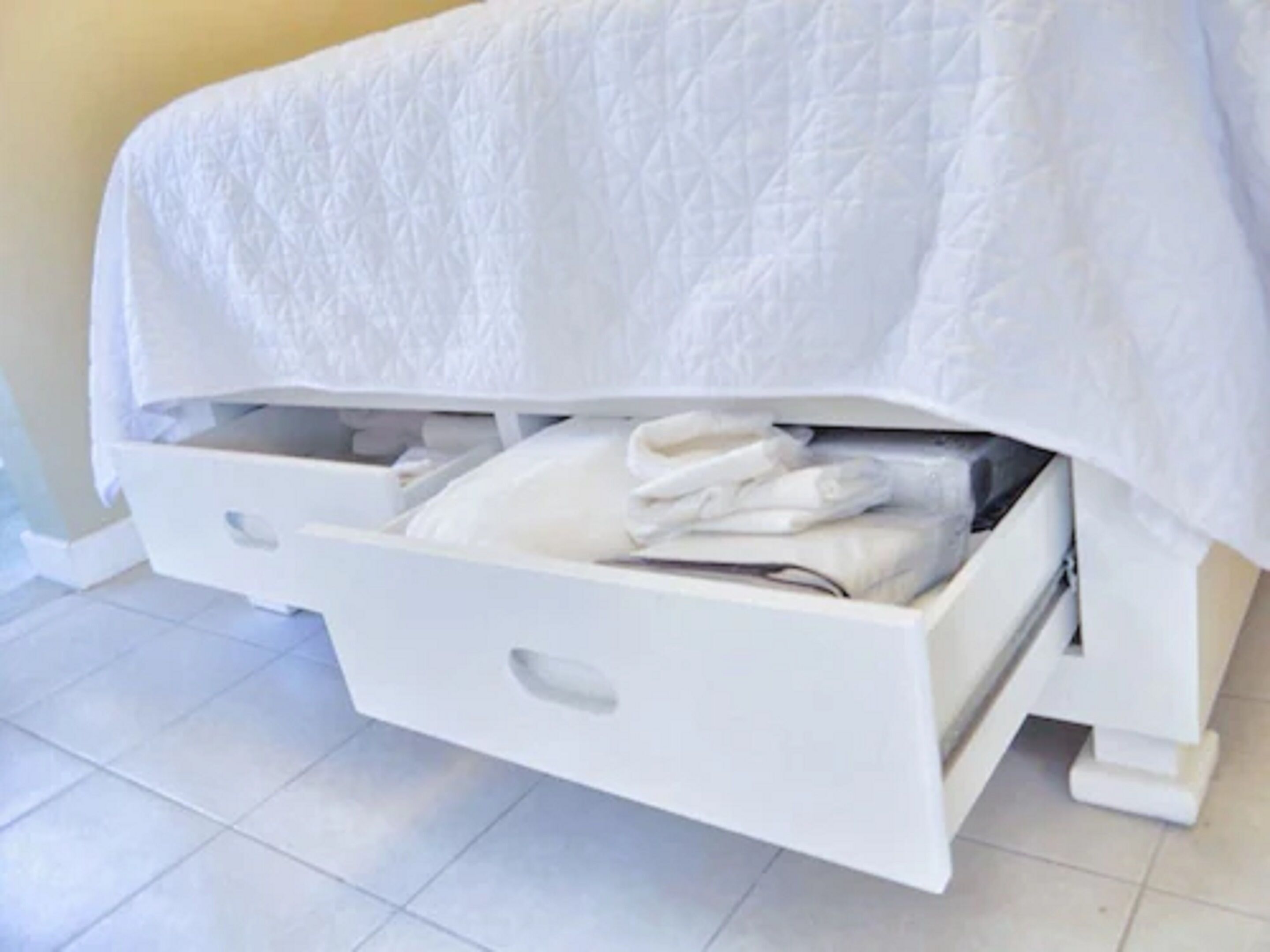 Un cassetto bianco sotto un letto, con asciugamani piegati.