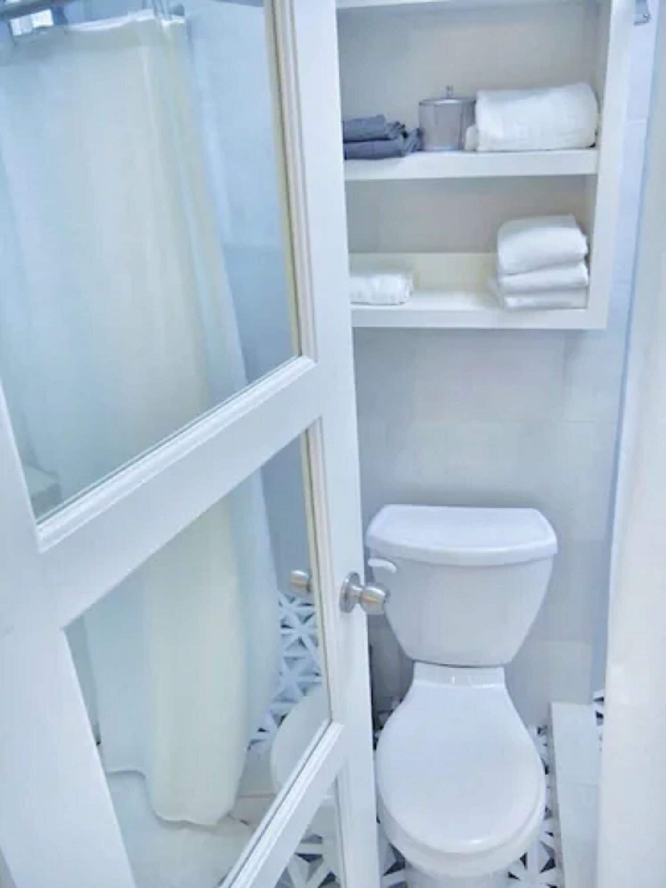 Ein Badezimmer mit Toilette, Duschvorhang und Regalen mit Handtüchern.