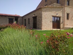 A stone building with a large glass door and windows, surrounded by a well-maintained lawn and flowering plants.