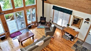 A cozy living room with a fireplace, wooden flooring, and large windows. - Stunning Cottage on a Very Private Lake (Kinmount)
