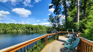 A wooden deck with a railing overlooking a lake, surrounded by dense forest. - Stunning Cottage on a Very Private Lake (Kinmount)