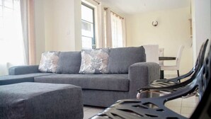 A modern living room with a grey sectional sofa, two patterned throw pillows, and a black metal chair. - The Mayal Homestay (Nairobi)