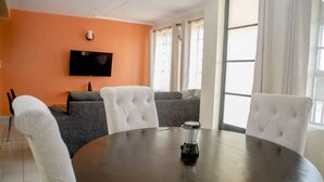 A modern living room with a round table, grey sofas, and a flat-screen TV mounted on an orange wall. - The Mayal Homestay (Nairobi)