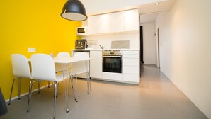 A compact kitchen with white cabinets, a black oven, and a microwave. There is a dining area with white chairs and a table. - The Sunny Reykjavik House (Reykjavik)