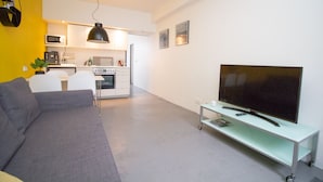A modern living room with a grey sofa, a TV on a white stand, and a kitchen in the background. - The Sunny Reykjavik House (Reykjavik)