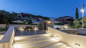 Eine Dachterrasse mit Stufen zu einer Sitzgelegenheit, Außenbeleuchtung und umgebenden Gebäuden.