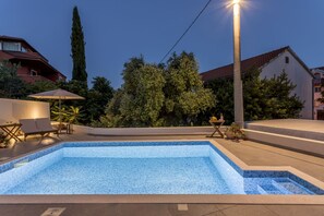 Ein Swimmingpool mit gefliesten Rändern, umgeben von einer Terrasse mit Liegestühlen und einem Tisch.