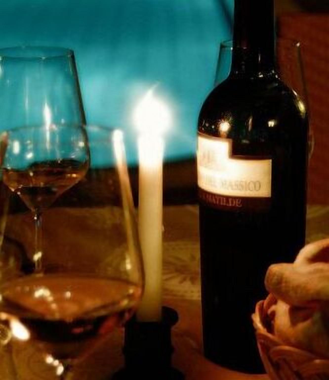 Una botella de vino, una vela encendida y un vaso sobre una mesa.