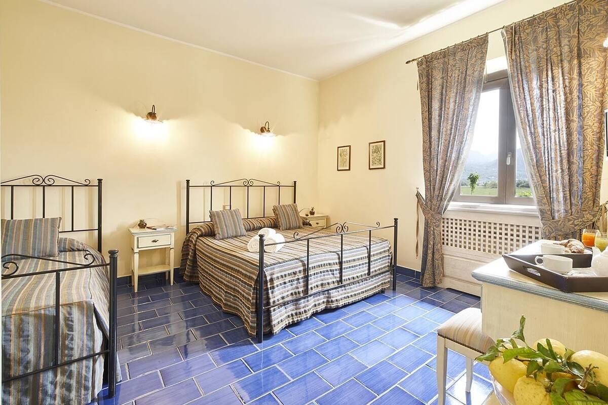 Un dormitorio con cama, mesitas de noche, ventana con cortinas y vistas al exterior.