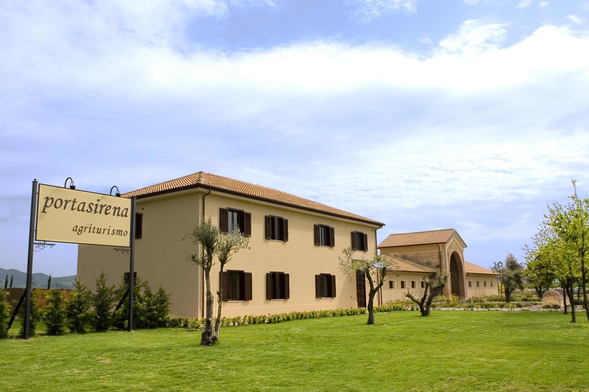 A large building with a sign reading "portasirena agriturismo" and a well-maintained lawn with trees.