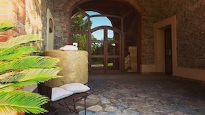 Un patio interior con suelo de piedra, una carretilla de madera con cojines y una gran bola de heno.
