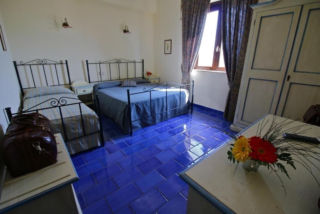 A room with two beds, a table with a vase of flowers, and a wardrobe.