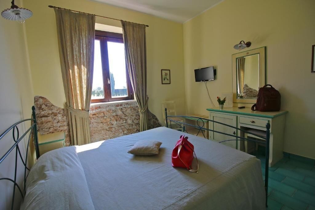 Une pièce comprenant un lit, un bureau, une chaise, un téléviseur et une fenêtre avec des rideaux.
