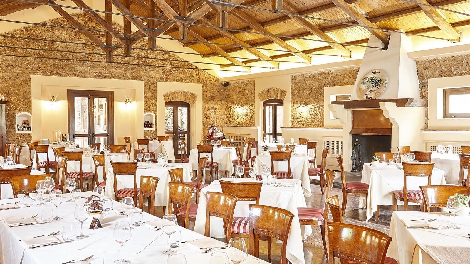 A spacious dining area with multiple tables and chairs, stone walls, and a high wooden ceiling.