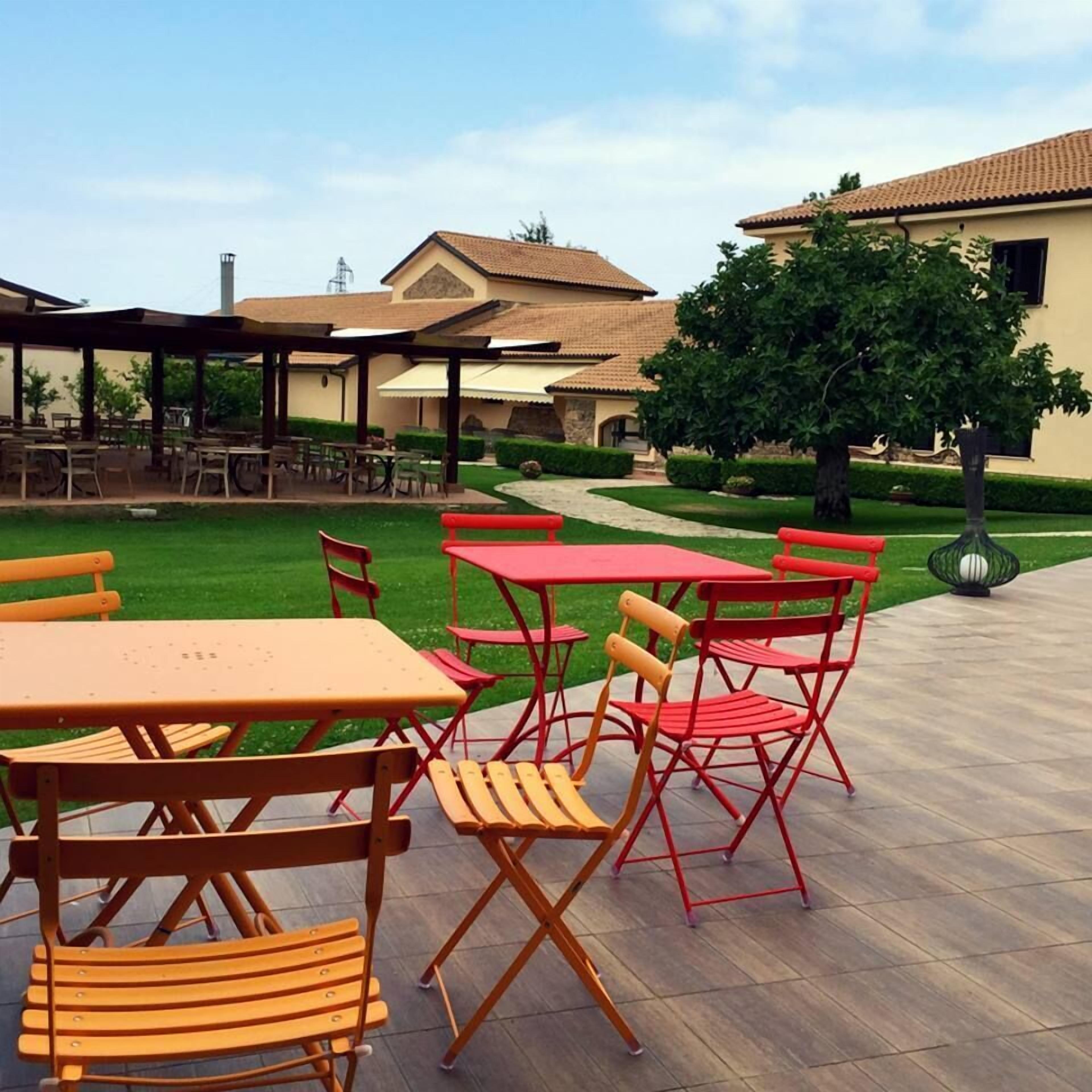 Un'area patio esterna con tavoli e sedie, un vialetto e un edificio sullo sfondo.