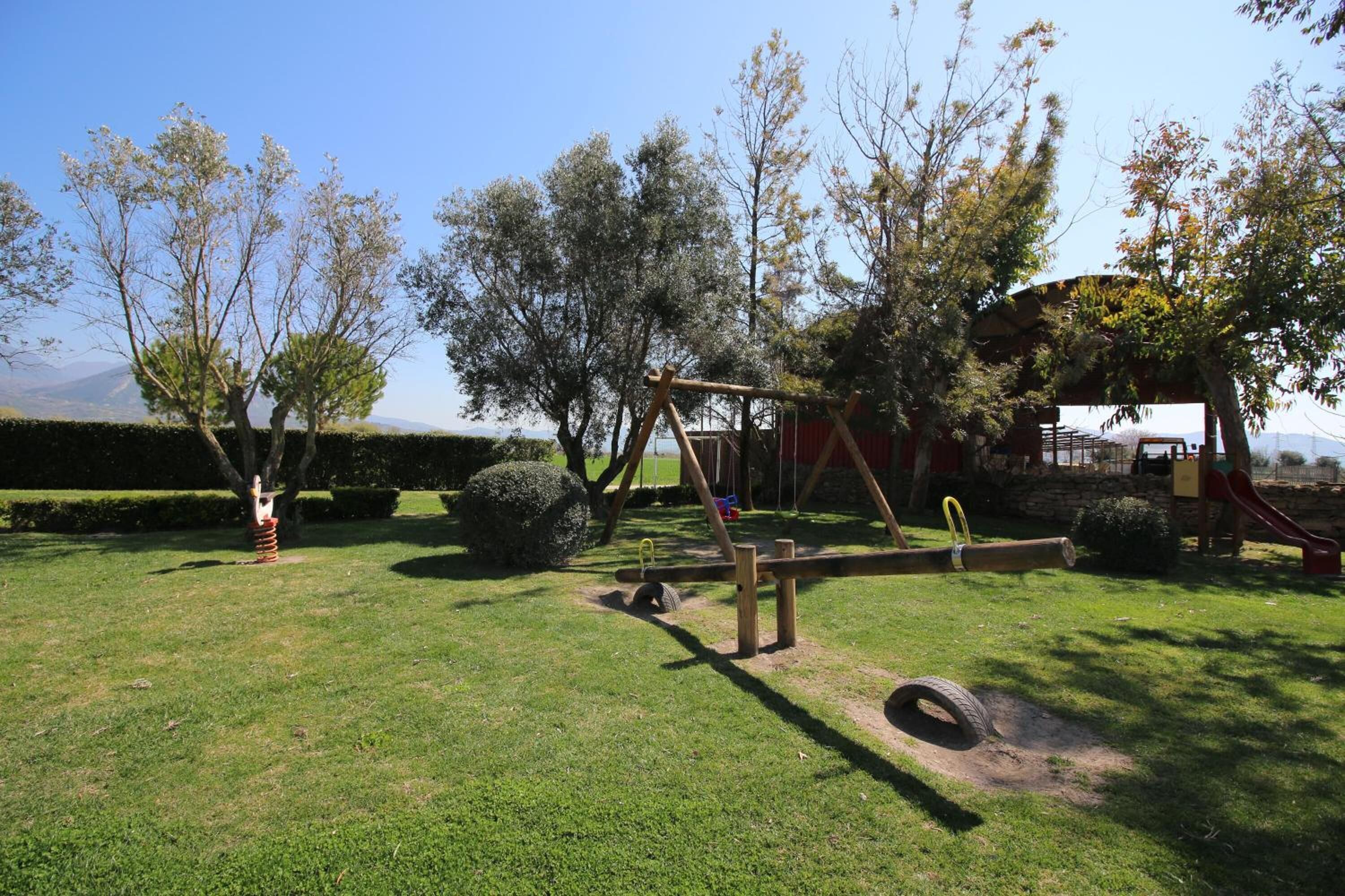 A playground with a swing set and a slide, surrounded by trees and a clear sky.