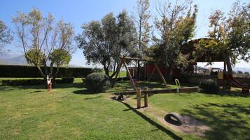 A playground with a swing set and a slide, surrounded by trees and a clear sky.