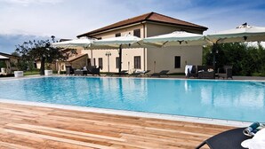 Una piscina con sillas de descanso y sombrillas, rodeada por una terraza de madera y un edificio con techo de tejas.