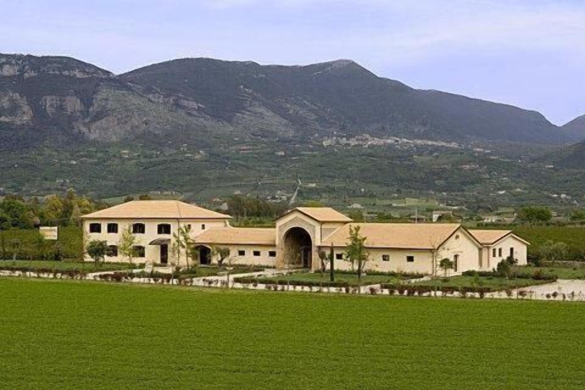 A building with a central arched entrance, surrounded by a well-maintained lawn and a mountainous backdrop.