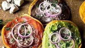 A variety of food items, including avocado slices topped with guacamole and red onion rings, arranged on a wooden surface.