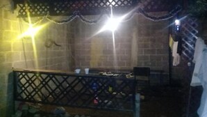 A patio area with a wooden fence, a table, and chairs. There are two light fixtures above the table.