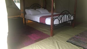 A four-poster bed with white linens and a plaid blanket, set in a tent-like room with a beige floor. - Kikopey Beach Camp (Gilgil)