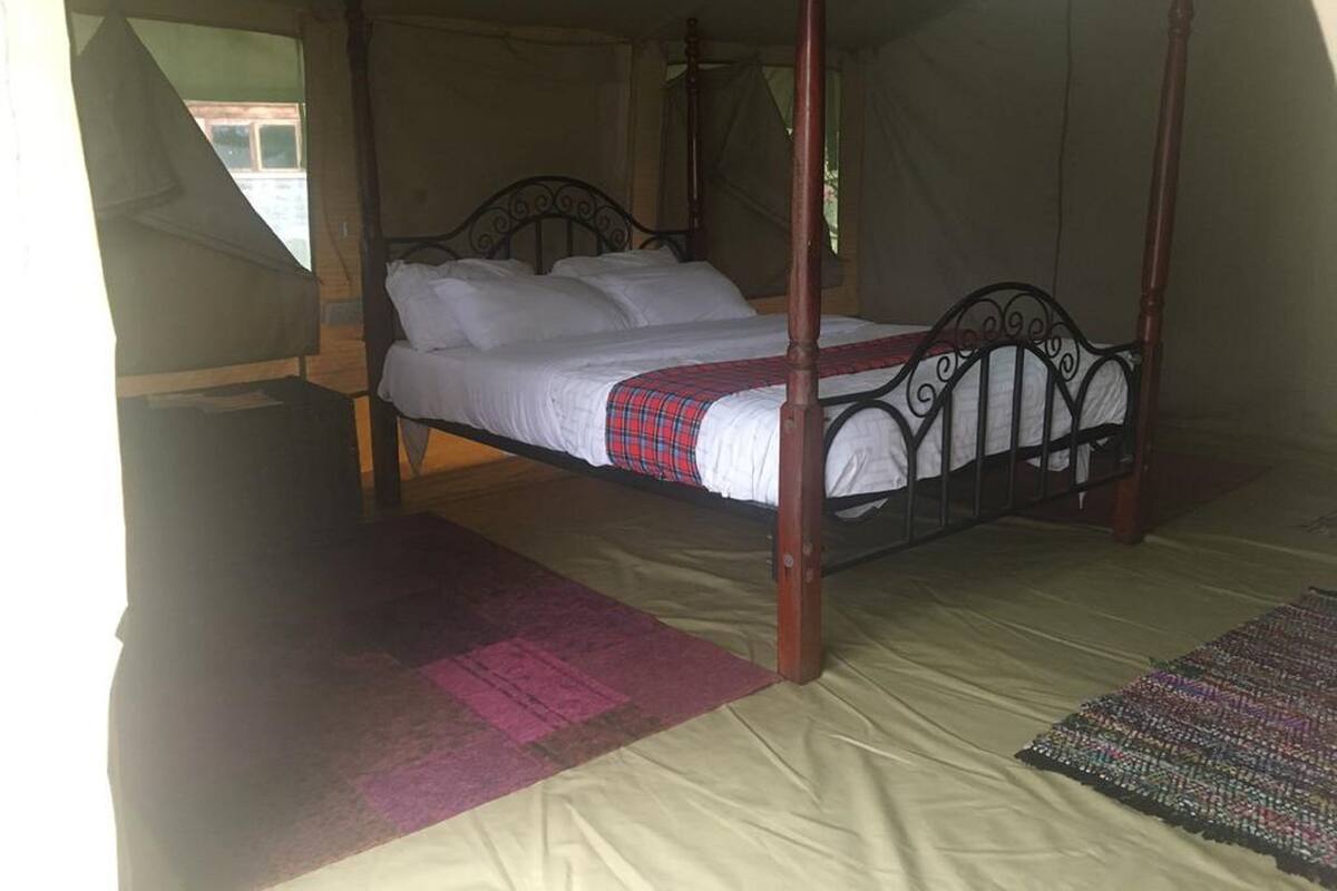 Uma cama de dossel com lençóis brancos e manta xadrez, em um quarto tipo tenda com piso bege.