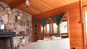 A cozy log cabin room with a stone fireplace, a sofa, and a large window with curtains. - Kikopey Beach Camp (Gilgil)