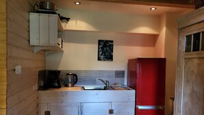 Uma cozinha compacta com armários de madeira, uma geladeira vermelha, uma cafeteira e uma chaleira.