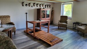 Quarto com mesa de centro de madeira, duas poltronas estampadas, um armário e caveiras de veado fixadas na parede.