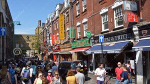 A busy street with pedestrians and a black car. - White's Row Resident (London)