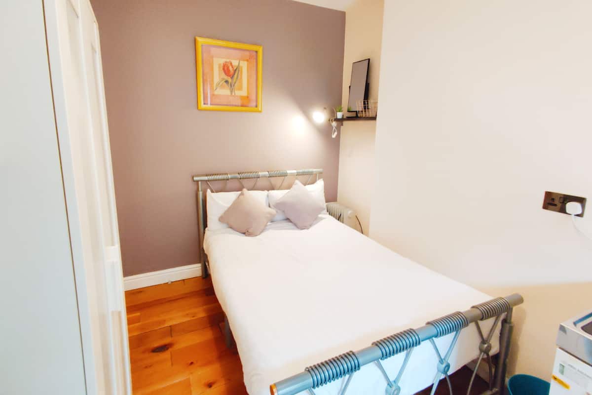 A bedroom with a bed, a headboard, a wall-mounted picture, and a small shelf.