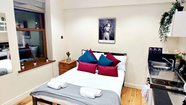 A hotel room with a bed, bedside table, and a small window. - White's Row Resident (London)