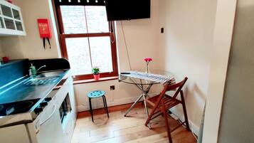 A kitchen with a stove, a sink, a small stool, a table with a keyboard, and a TV mounted on the wall.