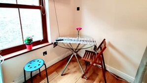 A corner room with a window, a small table with a striped tablecloth, a chair, a potted plant, and a TV mounted on the wall. - White's Row Resident (London)
