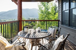 A wooden deck with a round table and chairs, overlooking a mountainous landscape. - Outpost: Grand View 5240 - AC and Teton Views (Jackson)