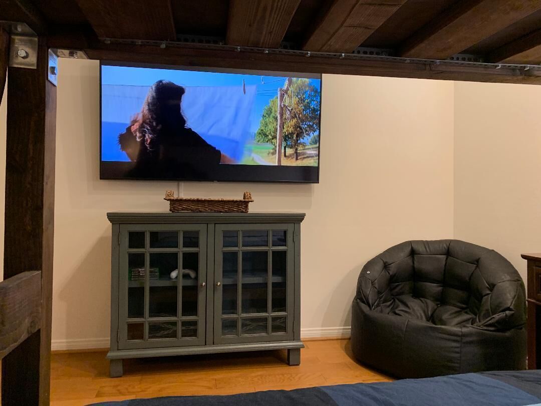 Une pièce avec un téléviseur fixé au mur, un meuble en bois foncé et un fauteuil en cuir noir en forme de sac.