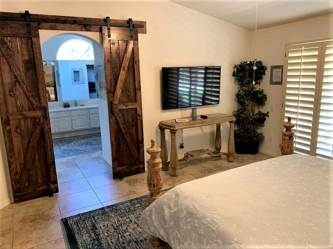 A bedroom with a bed, a TV, a wooden table, and a large mirror.