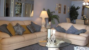 A living room with two beige sofas, a glass coffee table, and a blue shaggy carpet. - Sand Castle III Luxury Condo, Free nights for select dates. (Indian Shores)
