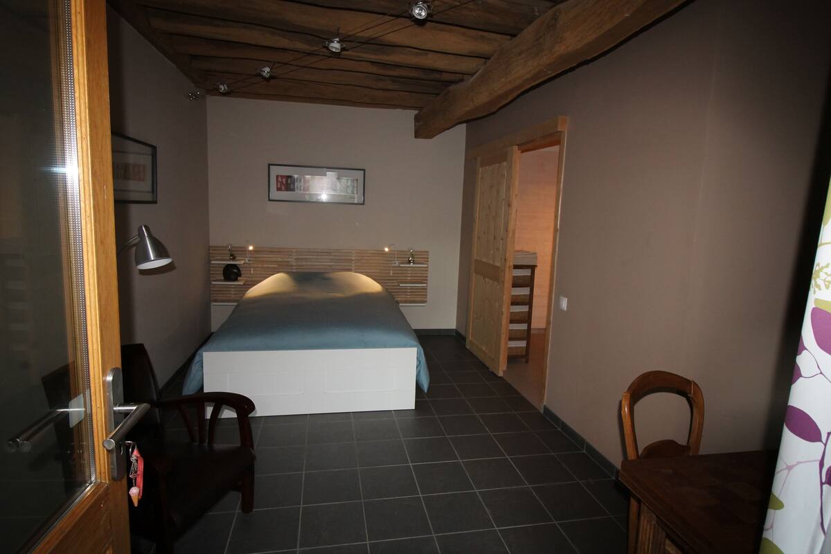Un dormitorio con cama, una silla, un escritorio, una lámpara y una puerta.