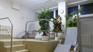 Un área de piscina interior moderna con vista despejada, un conjunto de escalones, sillones de descanso y plantas en macetas.