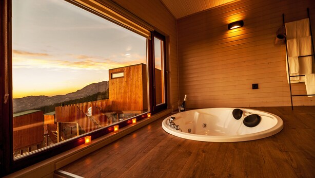 A modern bathroom with a large bathtub, wooden flooring, and a view of mountains through a large window. - Nidos de Carnota (Carnota)