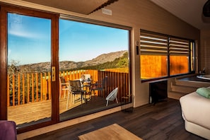Una habitación con un amplio ventanal corredizo que da a una terraza exterior con valla de madera y sillas.